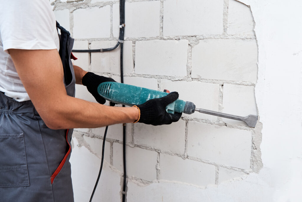 Man with demolition hammer remove stucco from wall. Renovation concept