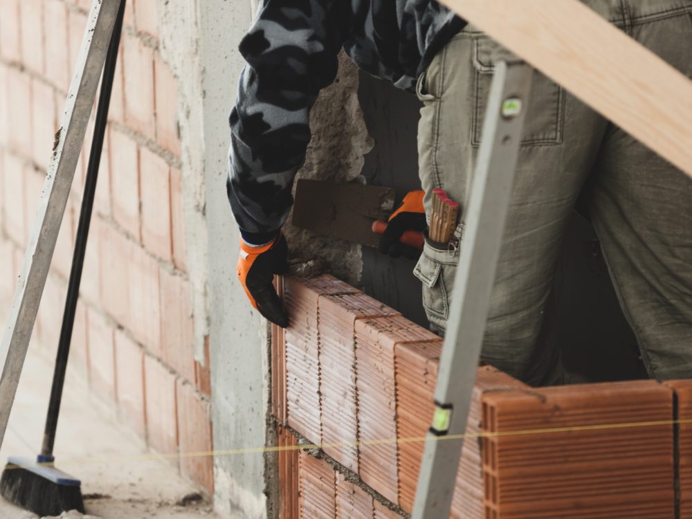 Bricklayer installing brick masonry on interior wall.